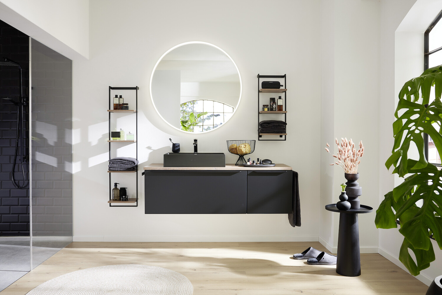 Modernes Bad mit rundem Spiegel und schwarzem Waschbecken.
