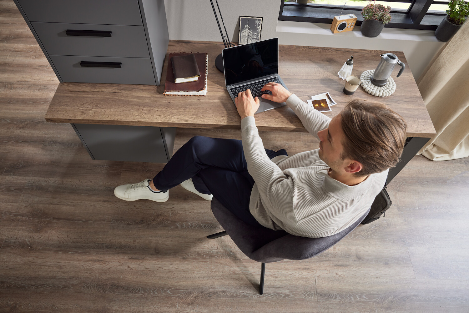 Blick auf einen Mann, der am Bürotisch mit seinem Laptop sitzt.