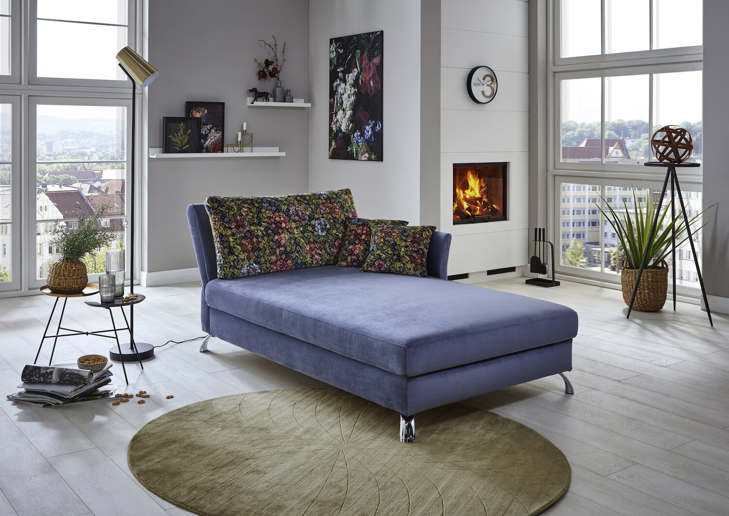 Blick auf ein Schlafsofa, Pflanzen, Regalen und Kaminfeuer.