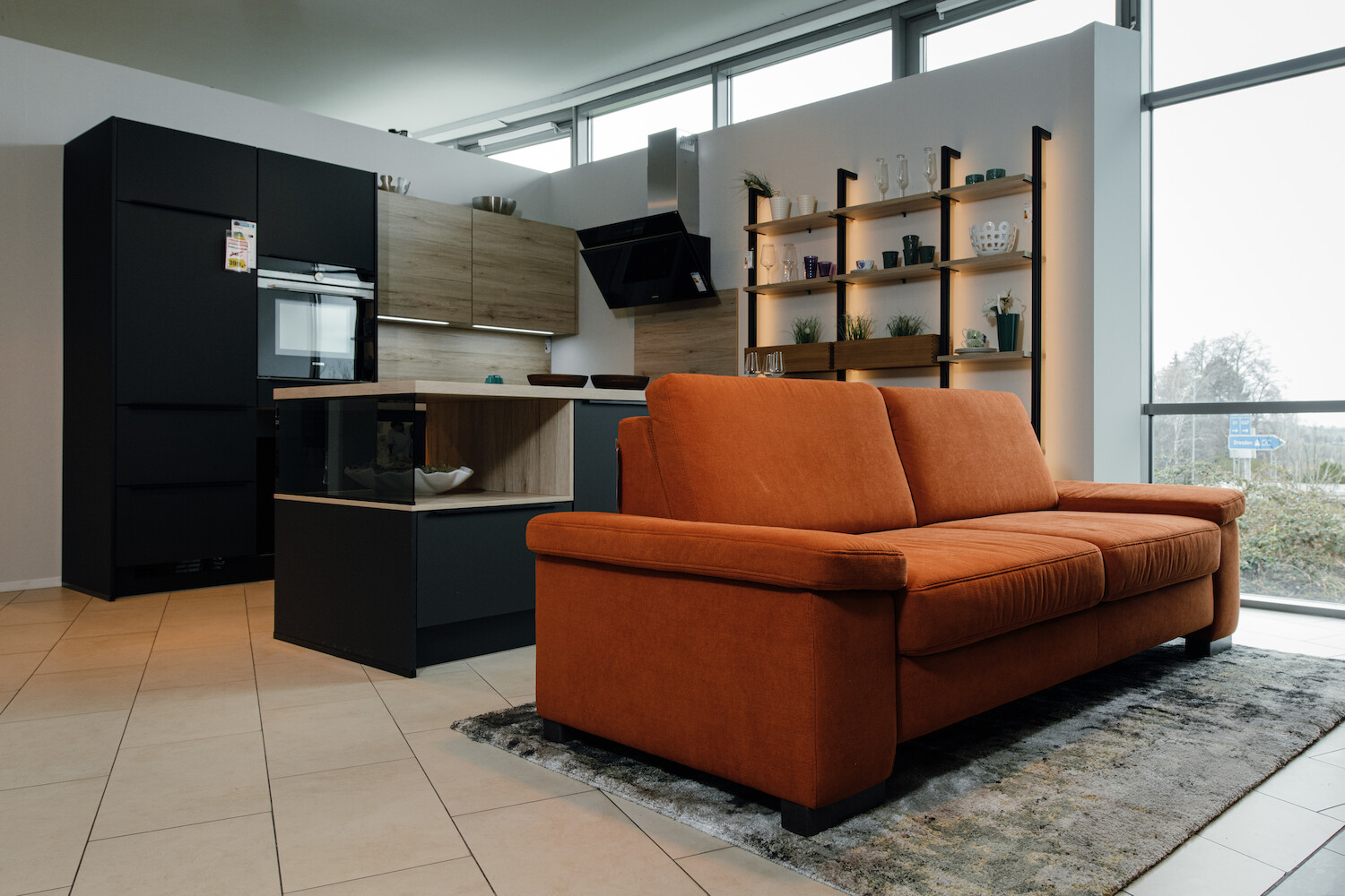 Im Hintergrund sieht man eine moderne Küche mit Kücheninsel, im Vordergrund eine Couch.